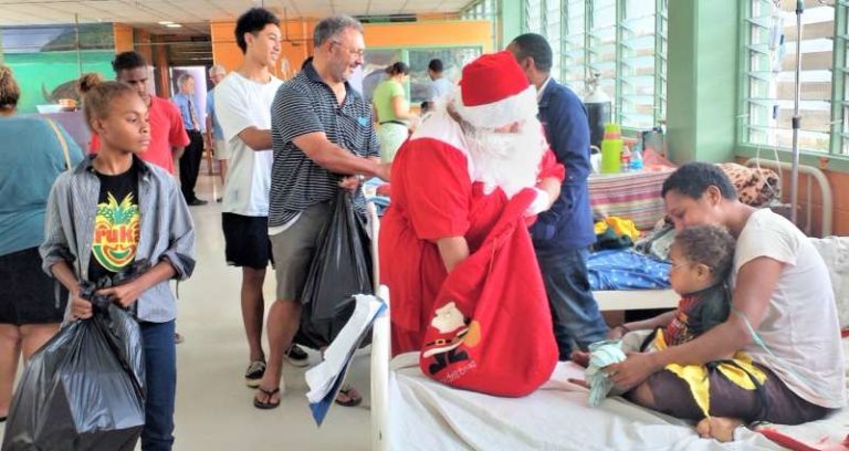 Image of Santa Claus accompanied by her helpers meets a child and her mother.